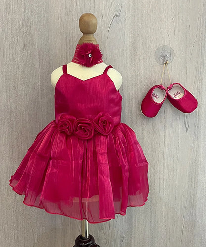 It’s a rani pink Colored dress that comes with a back zip closure. It is paired up with matching shoes and hair band. It features beautiful floral detailing on the waist and comes with a fabric belt to be tied at the back.