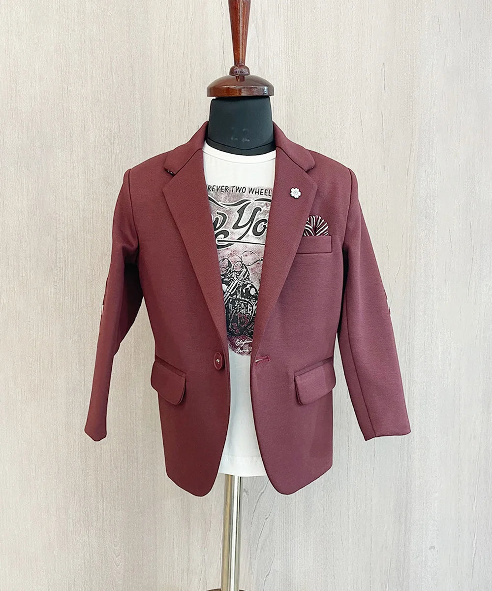 This boys wedding outfit consists of a Maroon Colored Blazer and a matching self-printed white Colored t-shirt. It features a small broach, a printed pocket square and elbow patch detailing that uplifts the entire look.