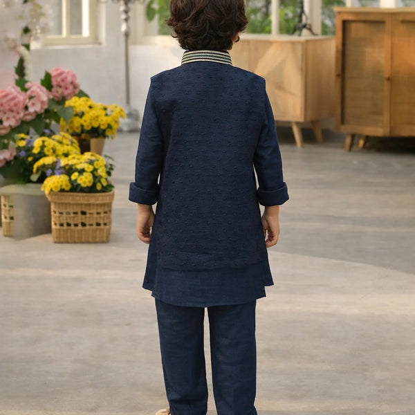 Child wearing a navy blue traditional outfit standing in a room with flowers and furniture.