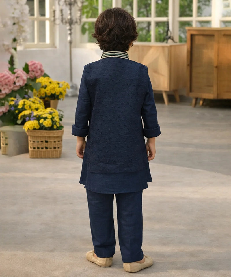 Child wearing a navy blue traditional outfit standing in a room with flowers and furniture.