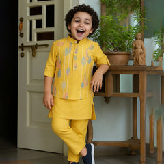 Child in a yellow outfit standing in a room with a wooden table and plants.