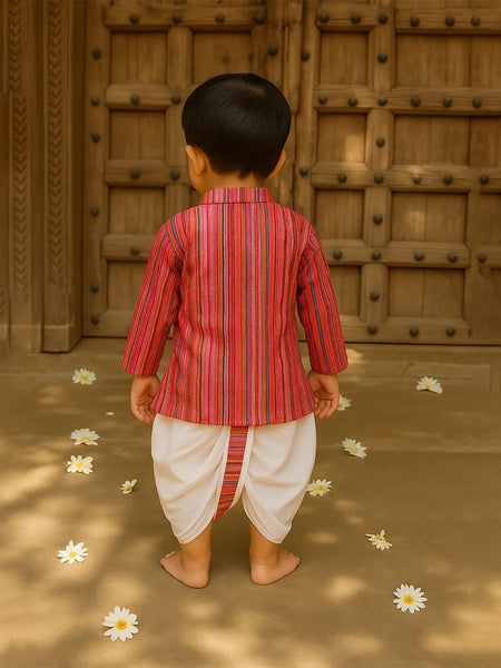 Child in a red and white striped traditional outfit standing in front of a wooden door with flowers on the ground.