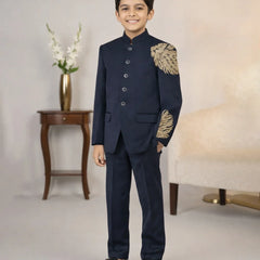 Young boy in a formal navy suit with gold embroidery standing in a room.