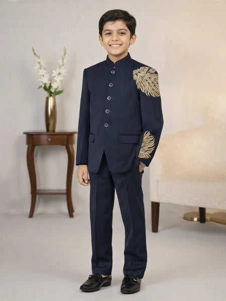 Young boy in a formal navy suit with gold embroidery standing in a room.