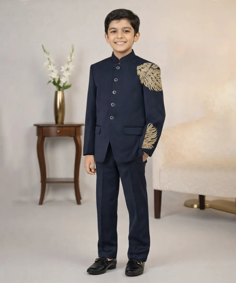 Young boy in a formal navy suit with gold embroidery standing in a room.