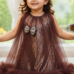 Young girl wearing a brown sequin dress with a bow, standing indoors.