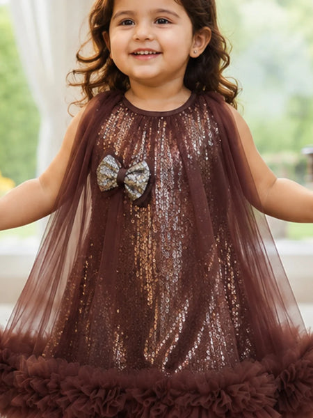 Young girl wearing a brown sequin dress with a bow, standing indoors.