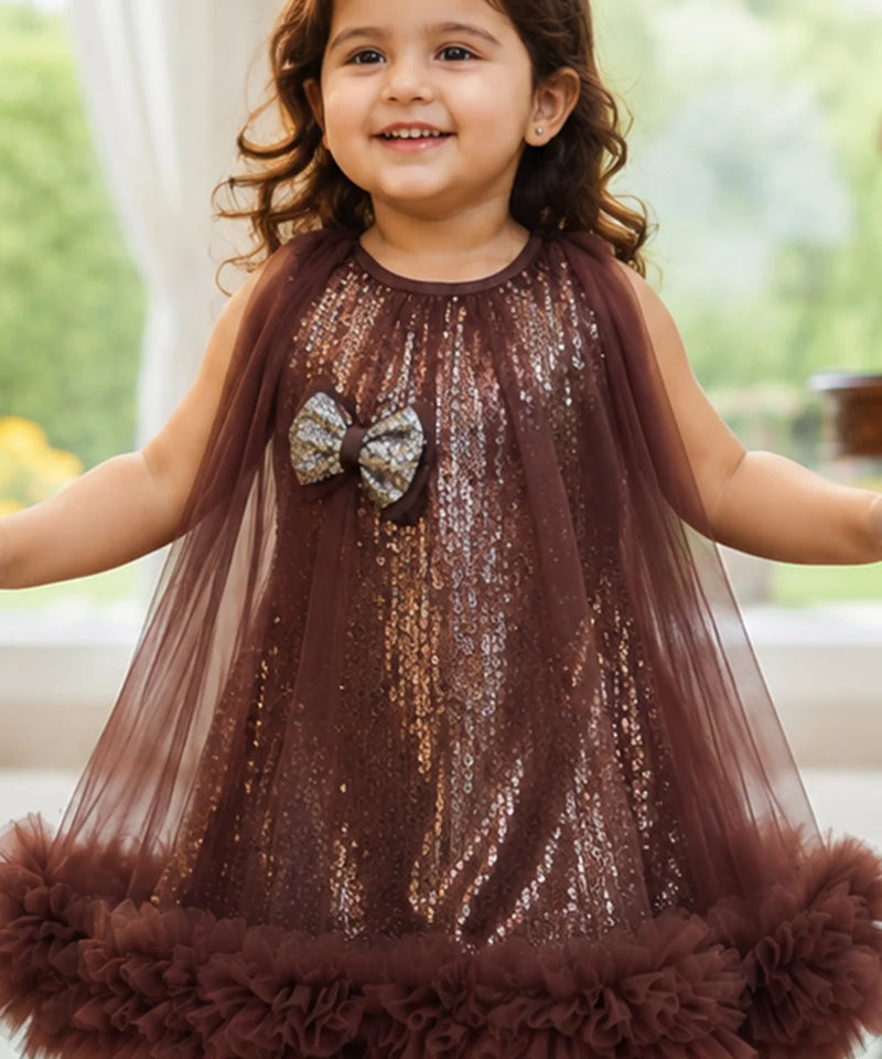 Young girl wearing a brown sequin dress with a bow, standing indoors.