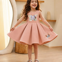 Young girl wearing a pink dress with butterfly designs indoors.