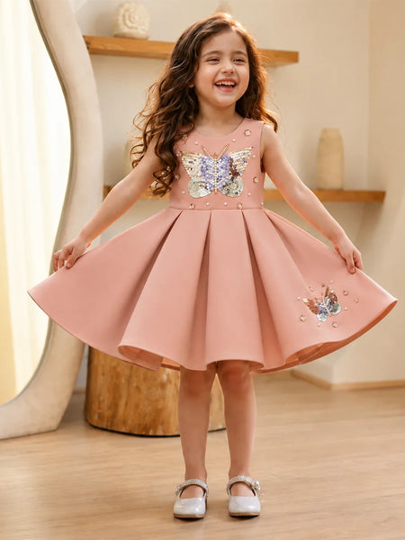 Young girl wearing a pink dress with butterfly designs indoors.