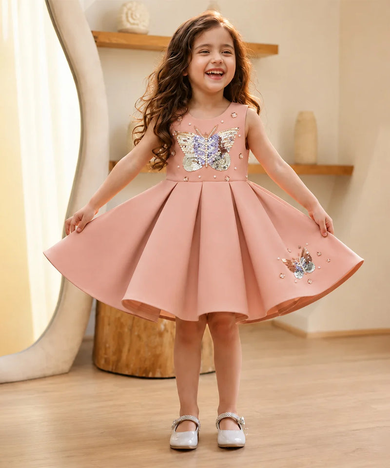 Young girl wearing a pink dress with butterfly designs indoors.
