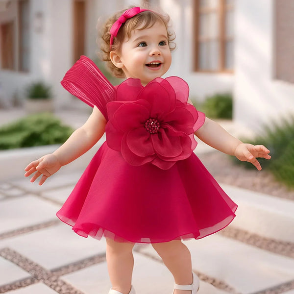 Child wearing a bright pink dress with a large flower on a stone path.