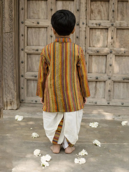 Child wearing a traditional striped kurta with white dhoti standing in front of a wooden door.
