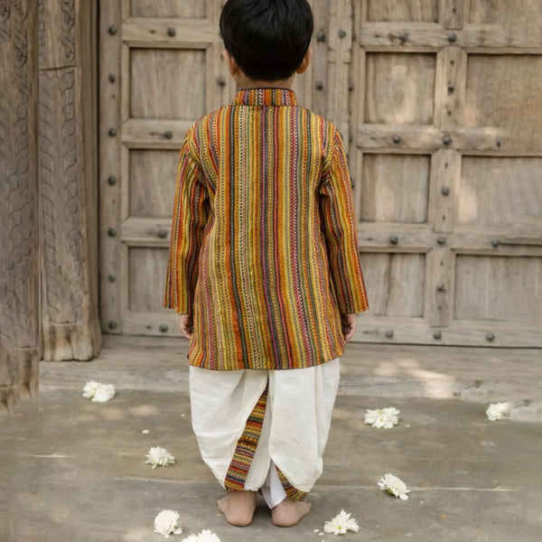 Child wearing a traditional striped kurta with white dhoti standing in front of a wooden door.