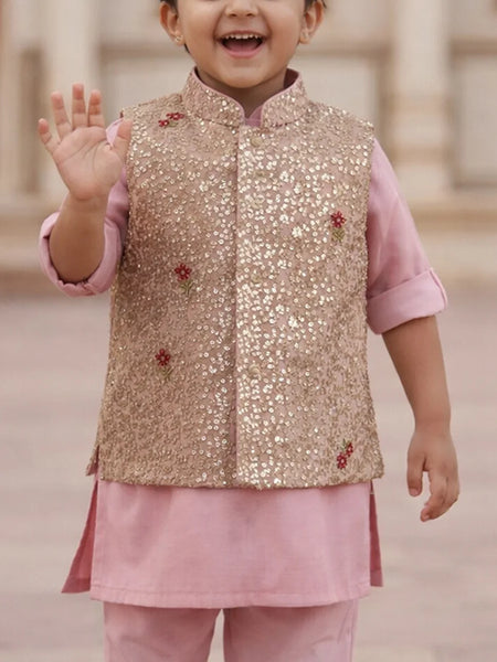Child wearing a gold sequined vest over a pink outfit with a blurred background