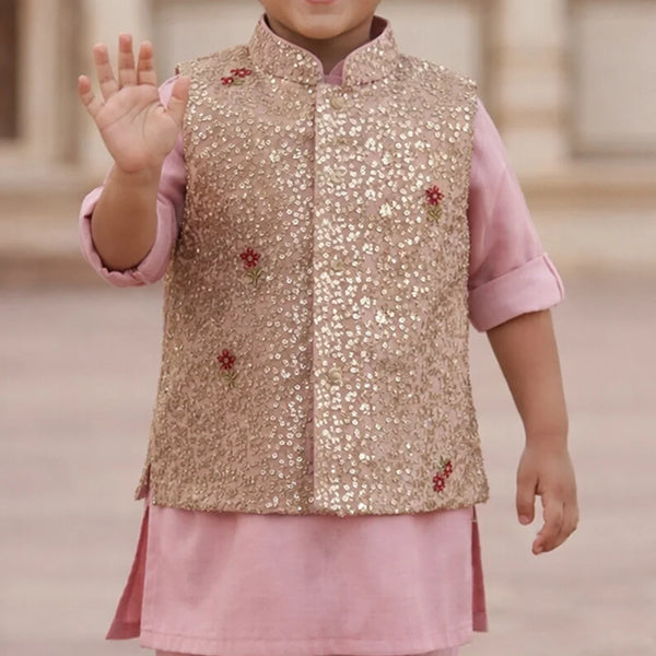 Child wearing a gold sequined vest over a pink outfit with a blurred background