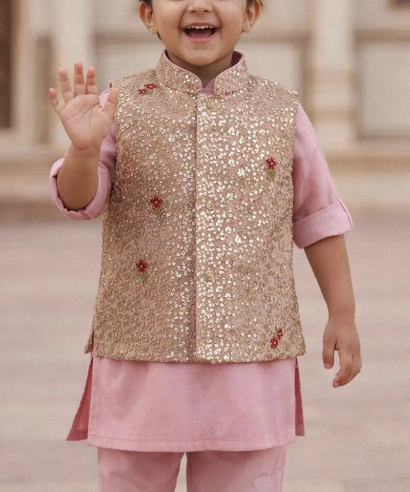 Child wearing a gold sequined vest over a pink outfit with a blurred background