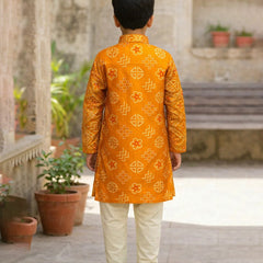 Child wearing a traditional orange kurta with white pants in an outdoor setting.