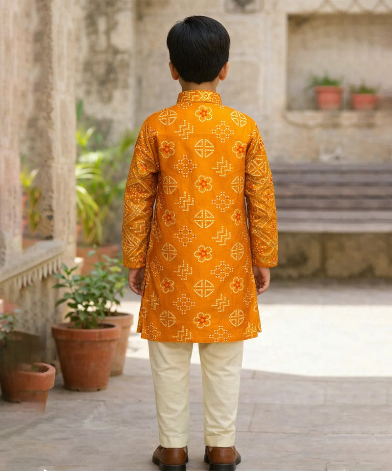 Child wearing a traditional orange kurta with white pants in an outdoor setting.
