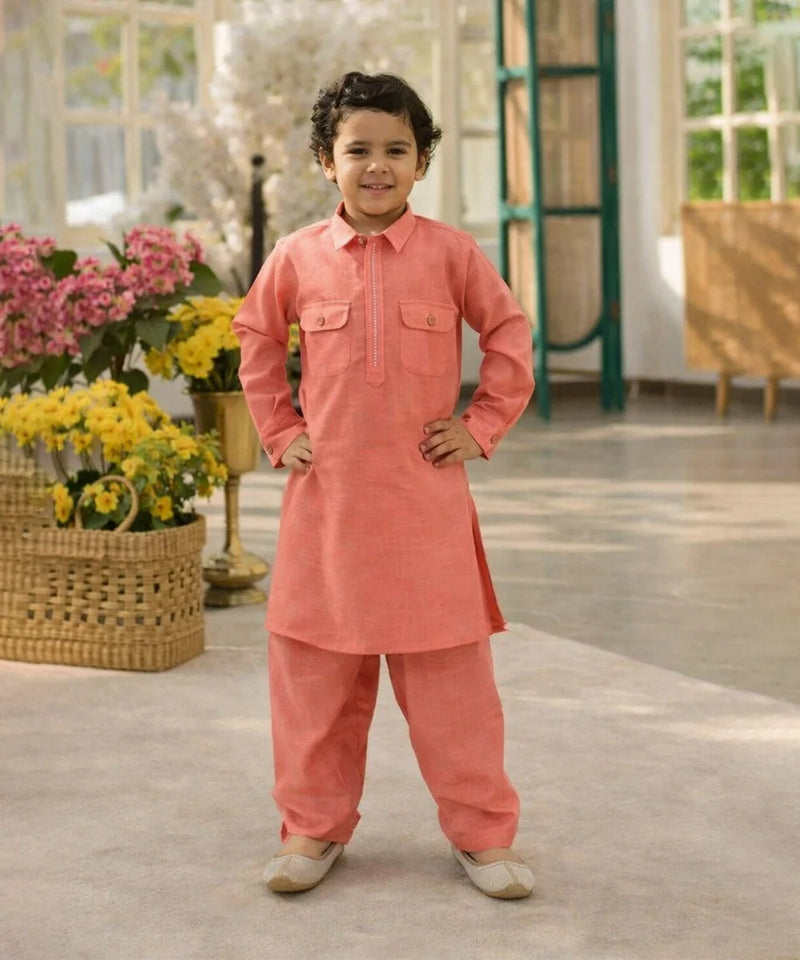 Child wearing a coral traditional outfit standing in a room with flowers and furniture.