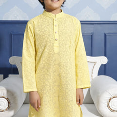 Child wearing a yellow kurta with white pants against a blue wall.