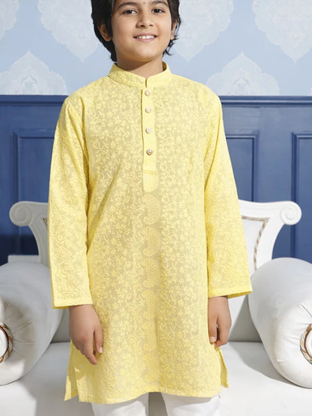 Child wearing a yellow kurta with white pants against a blue wall.