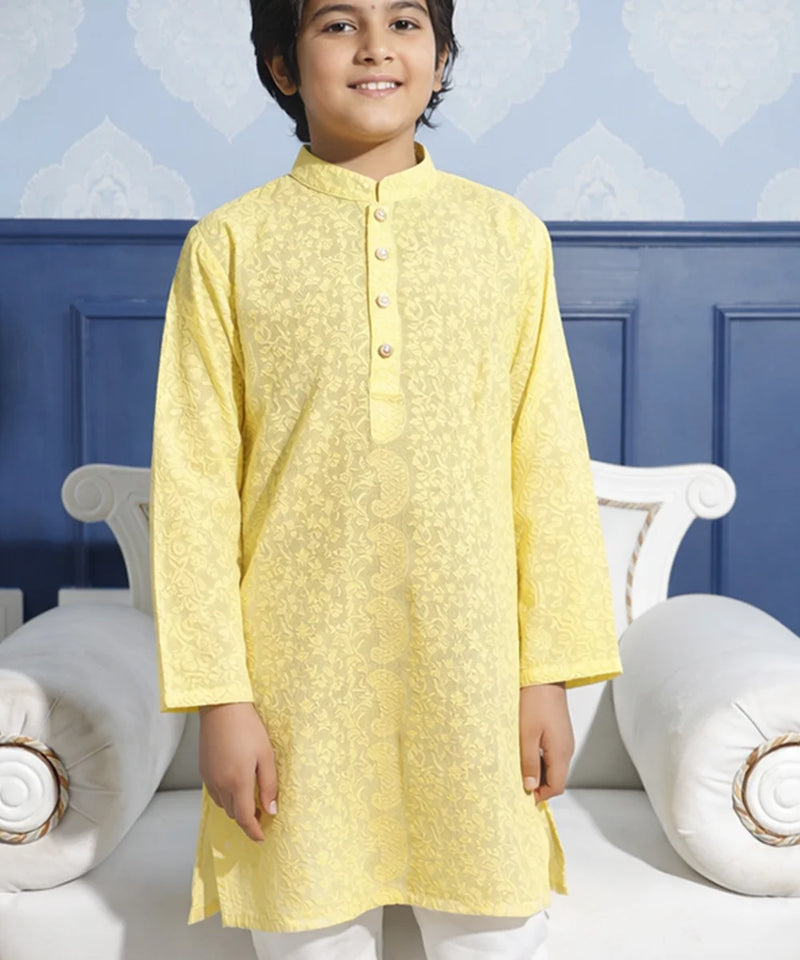 Child wearing a yellow kurta with white pants against a blue wall.