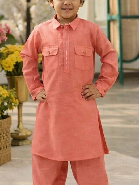 Child wearing a coral kurta with flowers and a green structure in the background