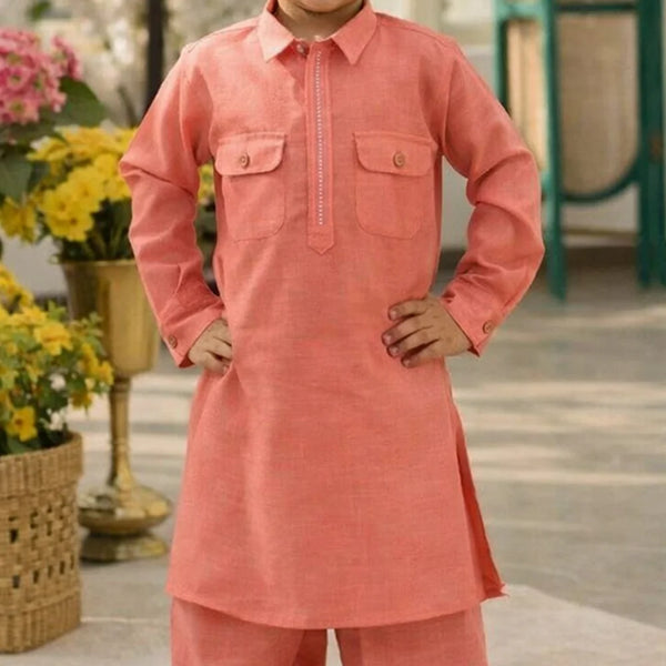Child wearing a coral kurta with flowers and a green structure in the background