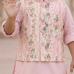 A child wearing a pink traditional outfit with a patterned vest featuring pink floral and geometric designs, set against a soft beige background.