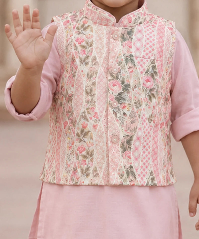 A child wearing a pink traditional outfit with a patterned vest featuring pink floral and geometric designs, set against a soft beige background.
