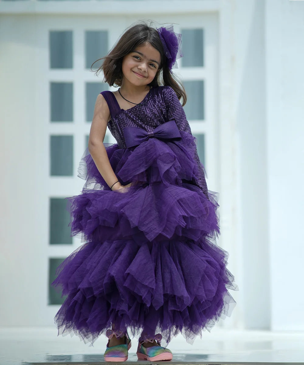 It's a fancy ruffle gown, in purple color that comes with a back zip closure. It features a beautiful big bow and fabric belt to be tied at the back.