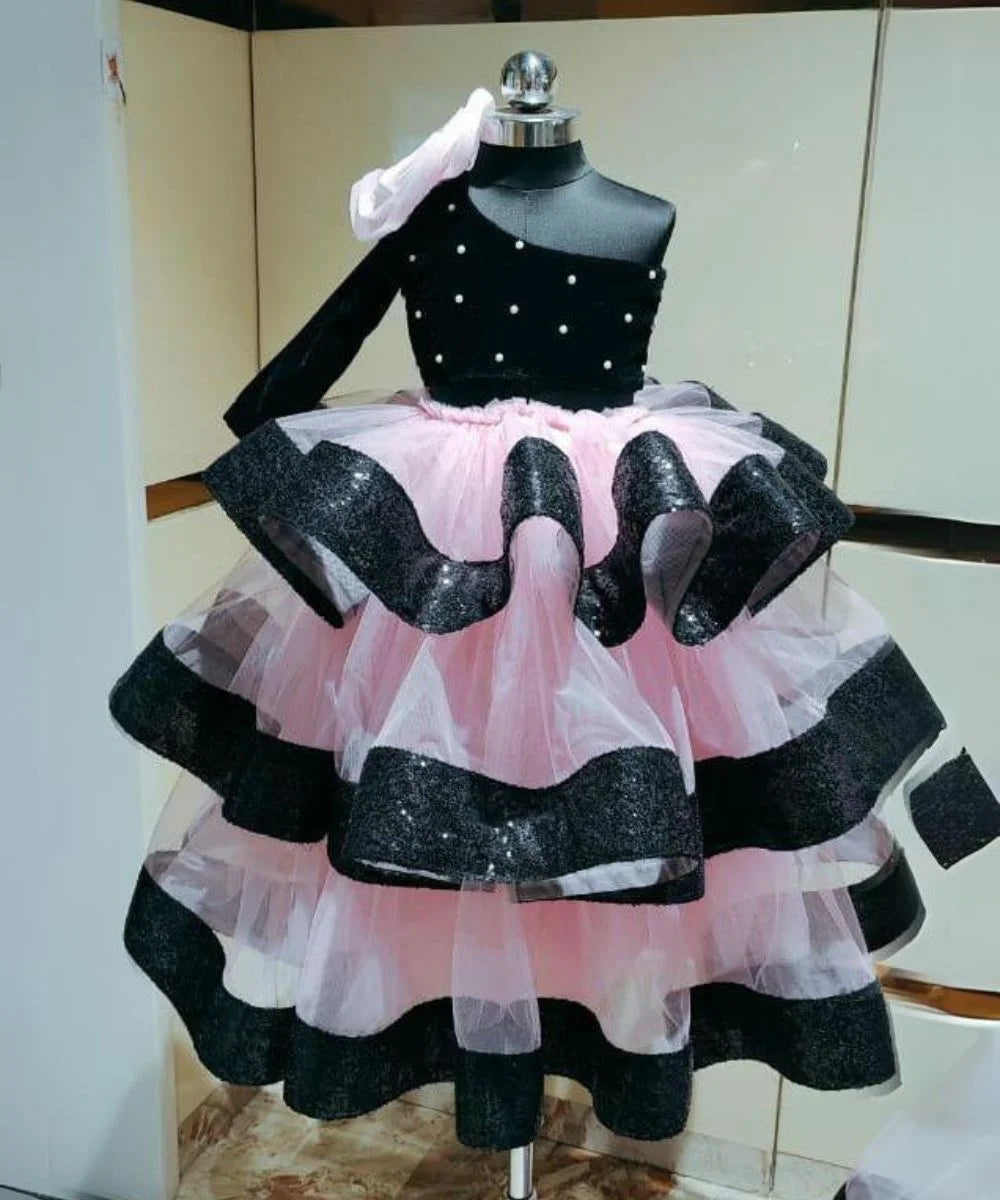 It’s a black and pink Colored one-shoulder ruffle gown for kid with a big floral and pearl detailing. 