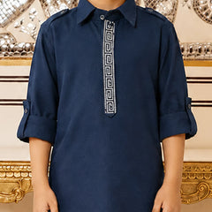 A child wearing a navy blue long-sleeve kurta with a white Greek key pattern down the center placket, standing in front of an ornate gold and silver mirror background.