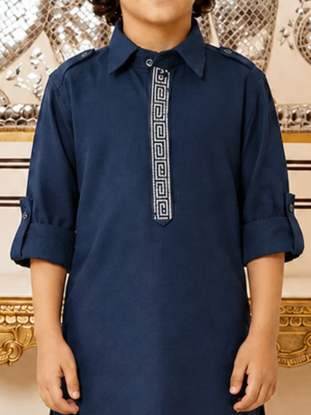A child wearing a navy blue long-sleeve kurta with a white Greek key pattern down the center placket, standing in front of an ornate gold and silver mirror background.