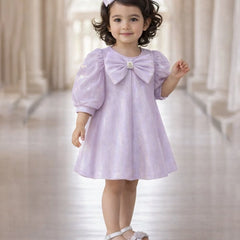 Young girl wearing a light purple dress with a large bow in a softly blurred indoor setting