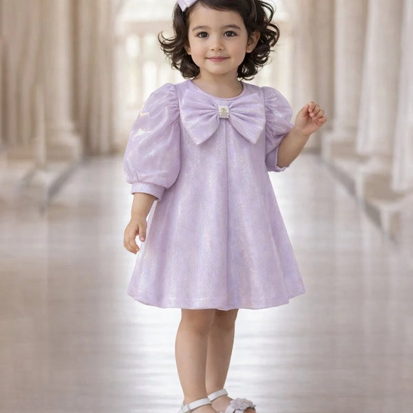 Young girl wearing a light purple dress with a large bow in a softly blurred indoor setting