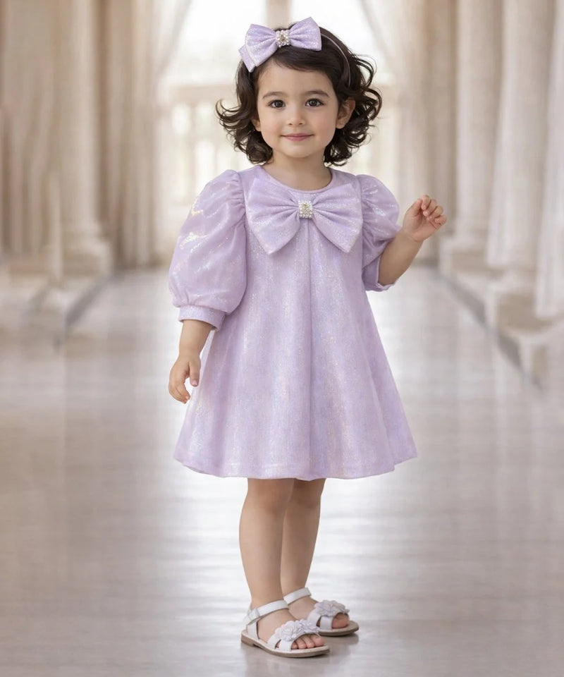 Young girl wearing a light purple dress with a large bow in a softly blurred indoor setting