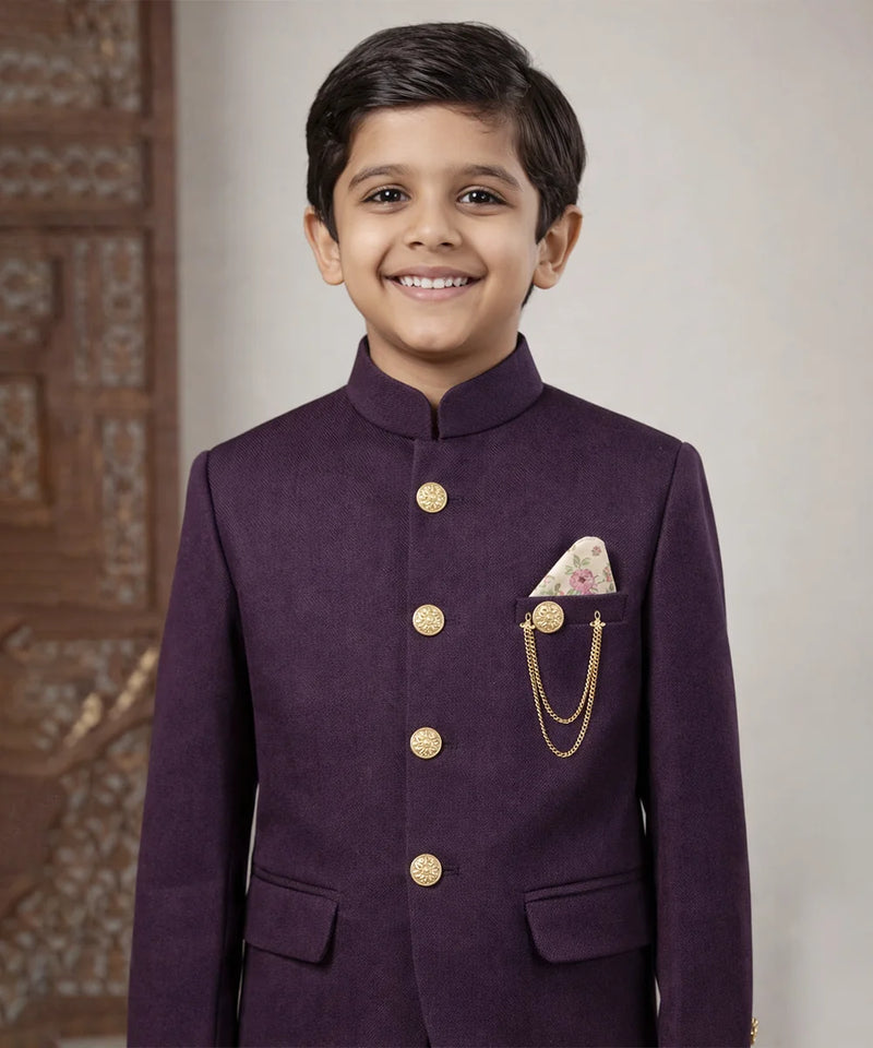 Young boy wearing a purple traditional outfit with gold buttons and a pocket square.