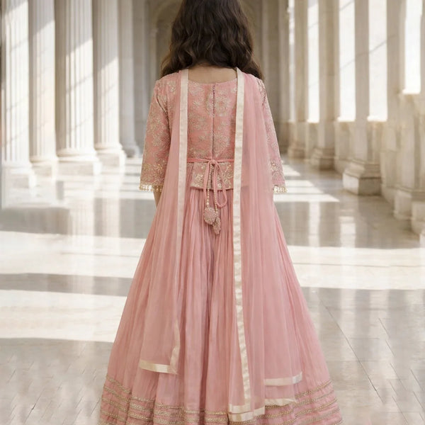 Woman in a pink traditional outfit standing in a sunlit architectural hallway.