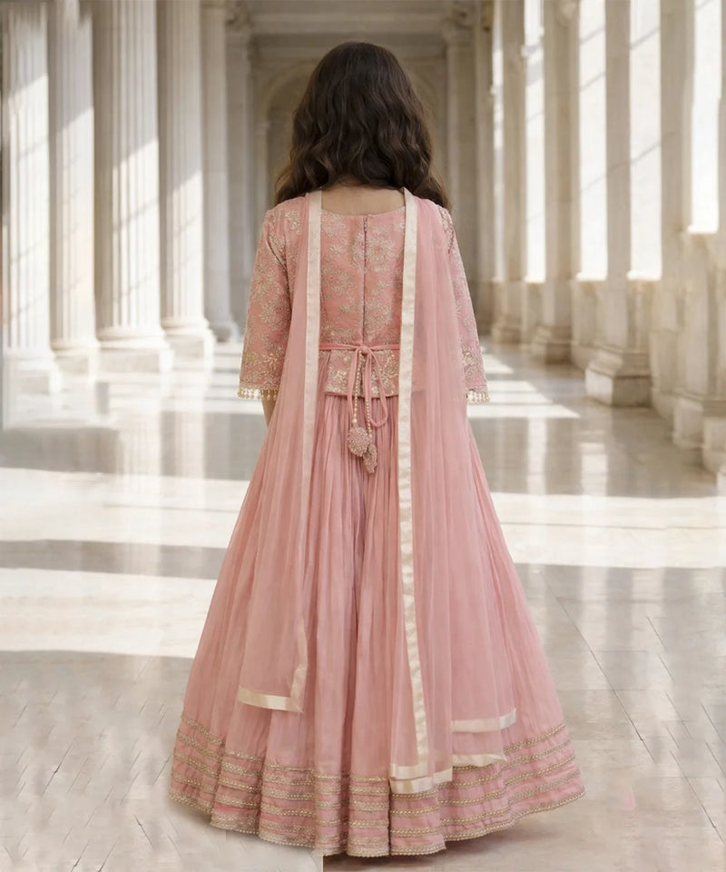 Woman in a pink traditional outfit standing in a sunlit architectural hallway.