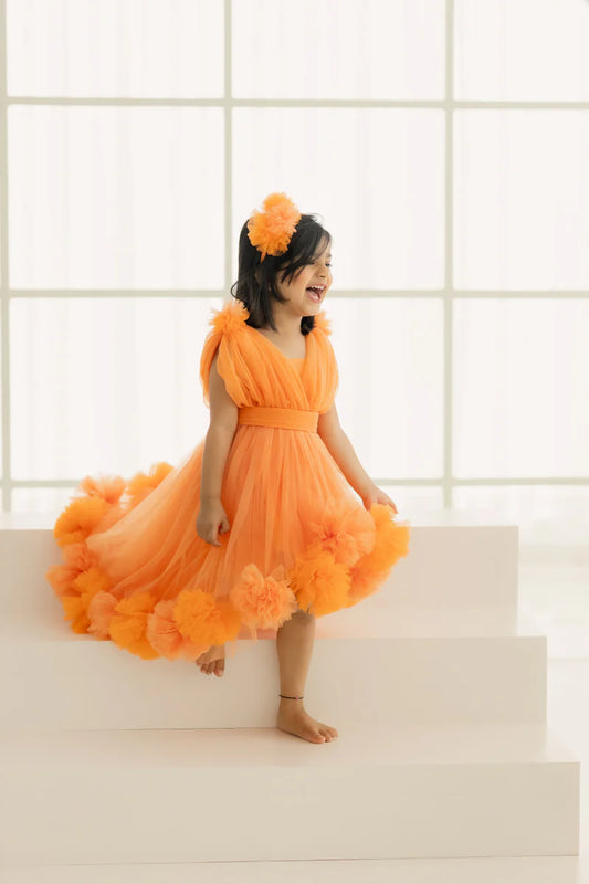 This orange coloured birthday party wear dress for kids has a back zip closure and comes with a matching belt. It features frilly floral detailing around the dress and on the shoulder that elevates the entire look.