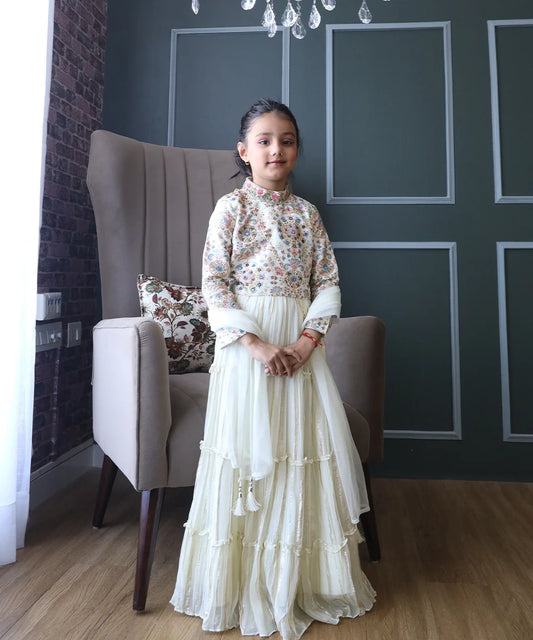 This Cream Colored  kids lehengas consist of an embroidered choli that comes with a back hook closure, a tiered skirt and a dupatta.