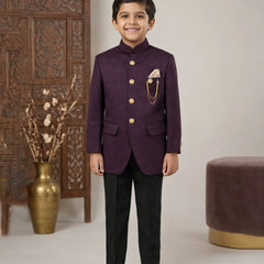 Young boy in a formal purple suit standing in a decorated room with a vase and decorative wall.
