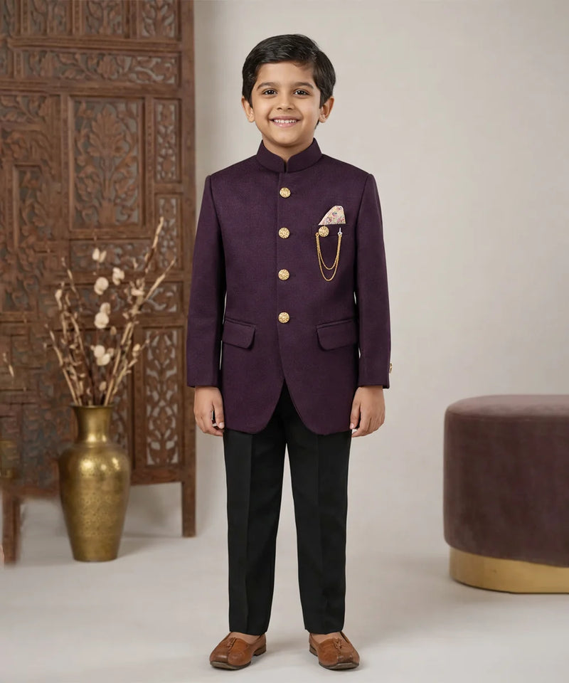 Young boy in a formal purple suit standing in a decorated room with a vase and decorative wall.