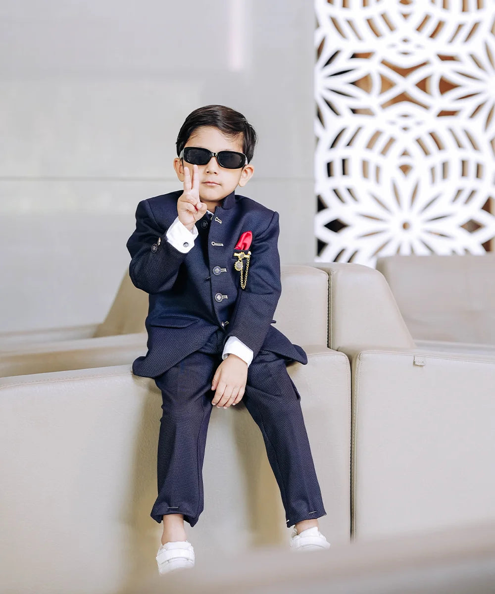 It is a beautiful navy blue coloured Jodhpuri suit for boys. It consists of a Jodhpuri Coat along with matching pants. It features a red coloured pocket square and a nice broach.