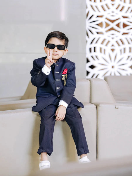 It is a beautiful navy blue coloured Jodhpuri suit for boys. It consists of a Jodhpuri Coat along with matching pants. It features a red coloured pocket square and a nice broach.