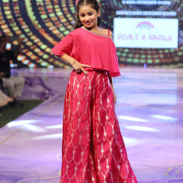 girl wearing a pink sharara outfit on a fashion show stage with a colorful background