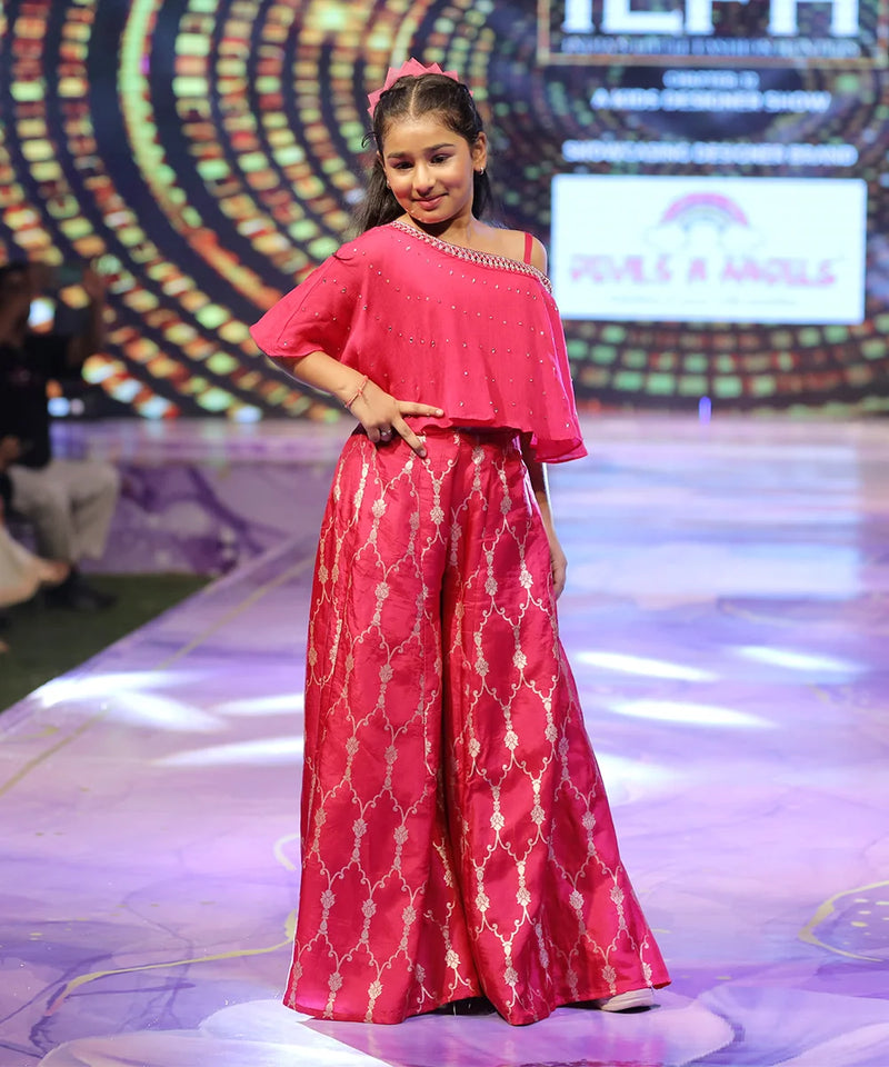 girl wearing a pink sharara outfit on a fashion show stage with a colorful background