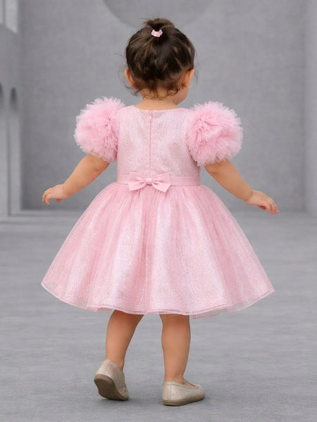 Child wearing a pink dress with fluffy sleeves on a gray background